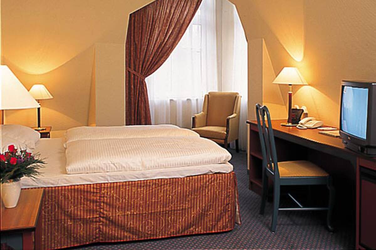 Une chambre d’hôtel avec un lit, deux chaises, un bureau avec un ordinateur et une télévision.