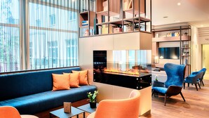 A modern living room with a blue sofa, orange armchairs, and a glass coffee table. - Welcome Hotel Marburg (Marburg)