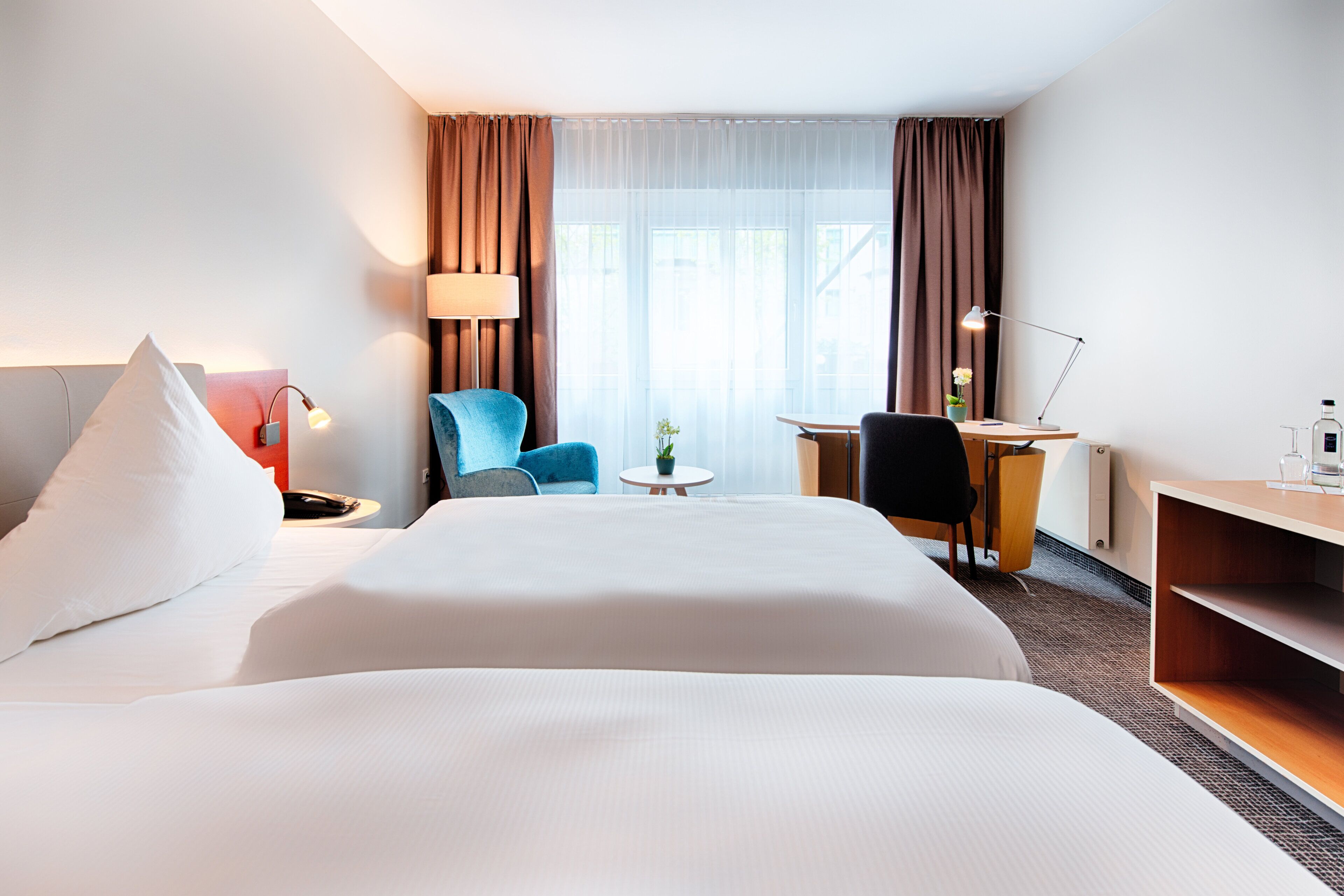Habitación de hotel con una cama grande, un escritorio, una silla, una lámpara y una pequeña mesa con una planta.