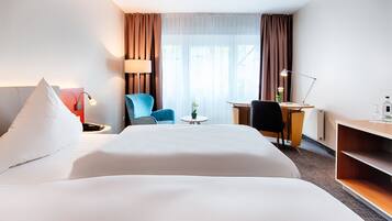 Habitación de hotel con una cama grande, un escritorio, una silla, una lámpara y una pequeña mesa con una planta.
