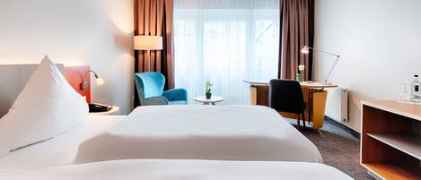Habitación de hotel con una cama grande, un escritorio, una silla, una lámpara y una pequeña mesa con una planta.