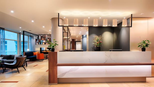 A modern reception area with a marble counter, potted plants, and a seating area with a sofa and chairs. - Welcome Hotel Marburg (Marburg)