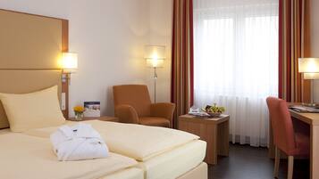 Une chambre d’hôtel comprenant un lit, deux chaises, un bureau, une petite table avec un panier de fruits et deux lampes.