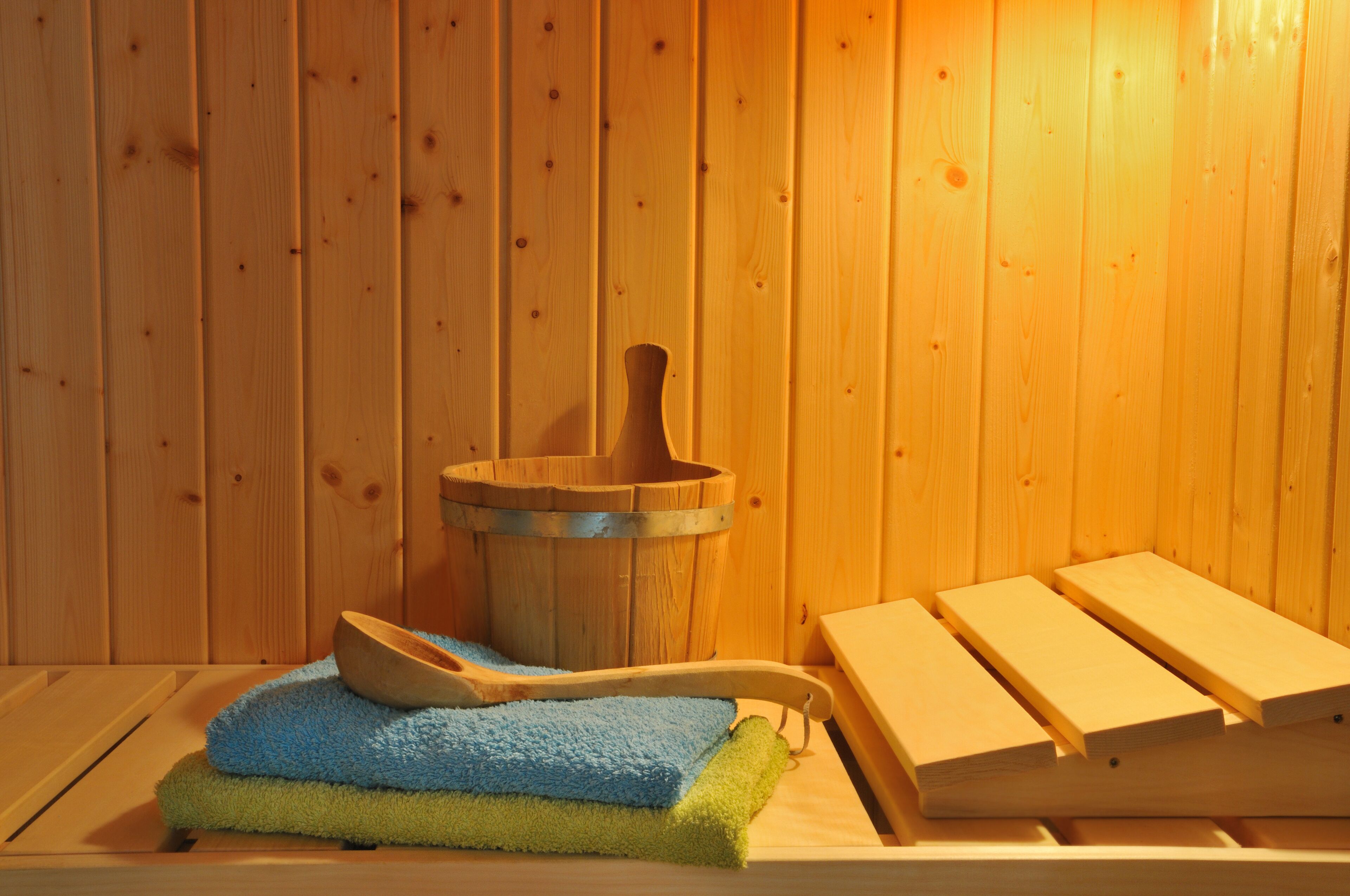 Eine Holzsauna mit einem Holzeimer, einem blaugrünen Handtuch und Holzsitzen.