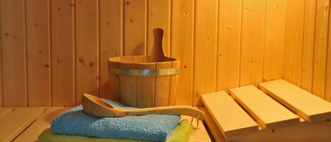 Eine Holzsauna mit einem Holzeimer, einem blaugrünen Handtuch und Holzsitzen.