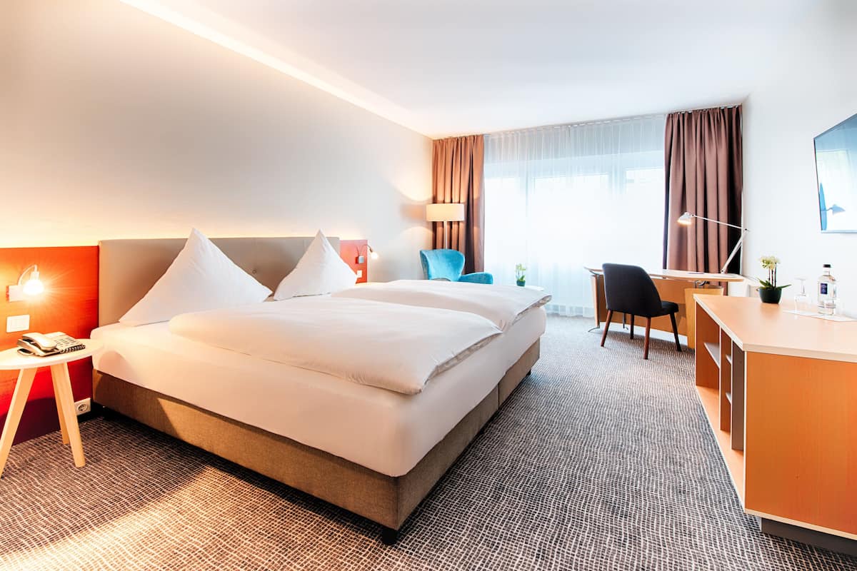 Ein Hotelzimmer mit einem großen Bett, einem Schreibtisch, einem Sessel und einer Lampe.