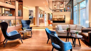 A modern hotel lobby with seating areas, a fireplace, and a view of the outside. - Welcome Hotel Marburg (Marburg)
