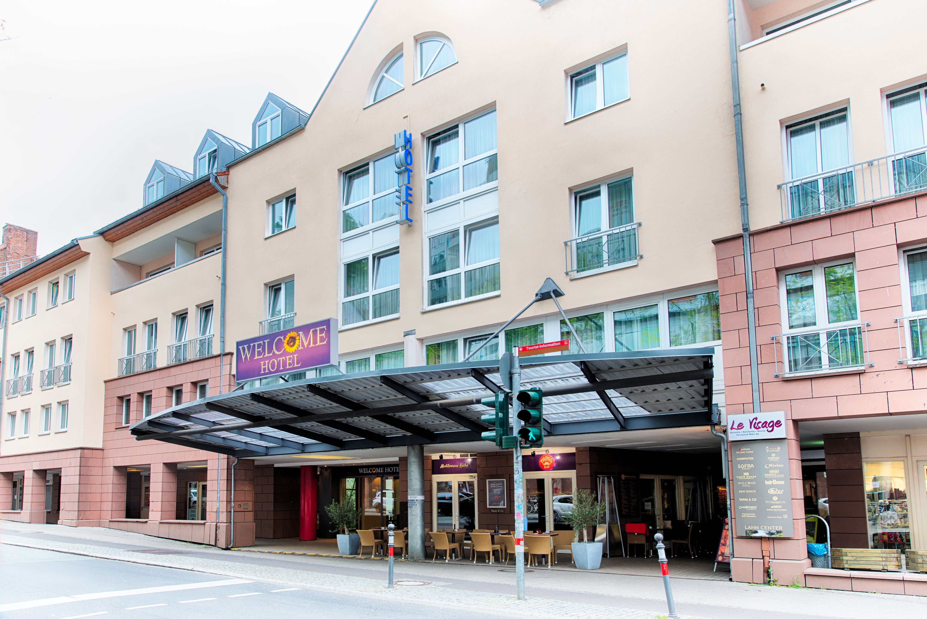 A hotel with a covered entrance, outdoor seating area, and a sign for 'Le Vigue'.