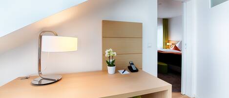 A modern hotel room with a desk, a lamp, a phone, and a small plant.