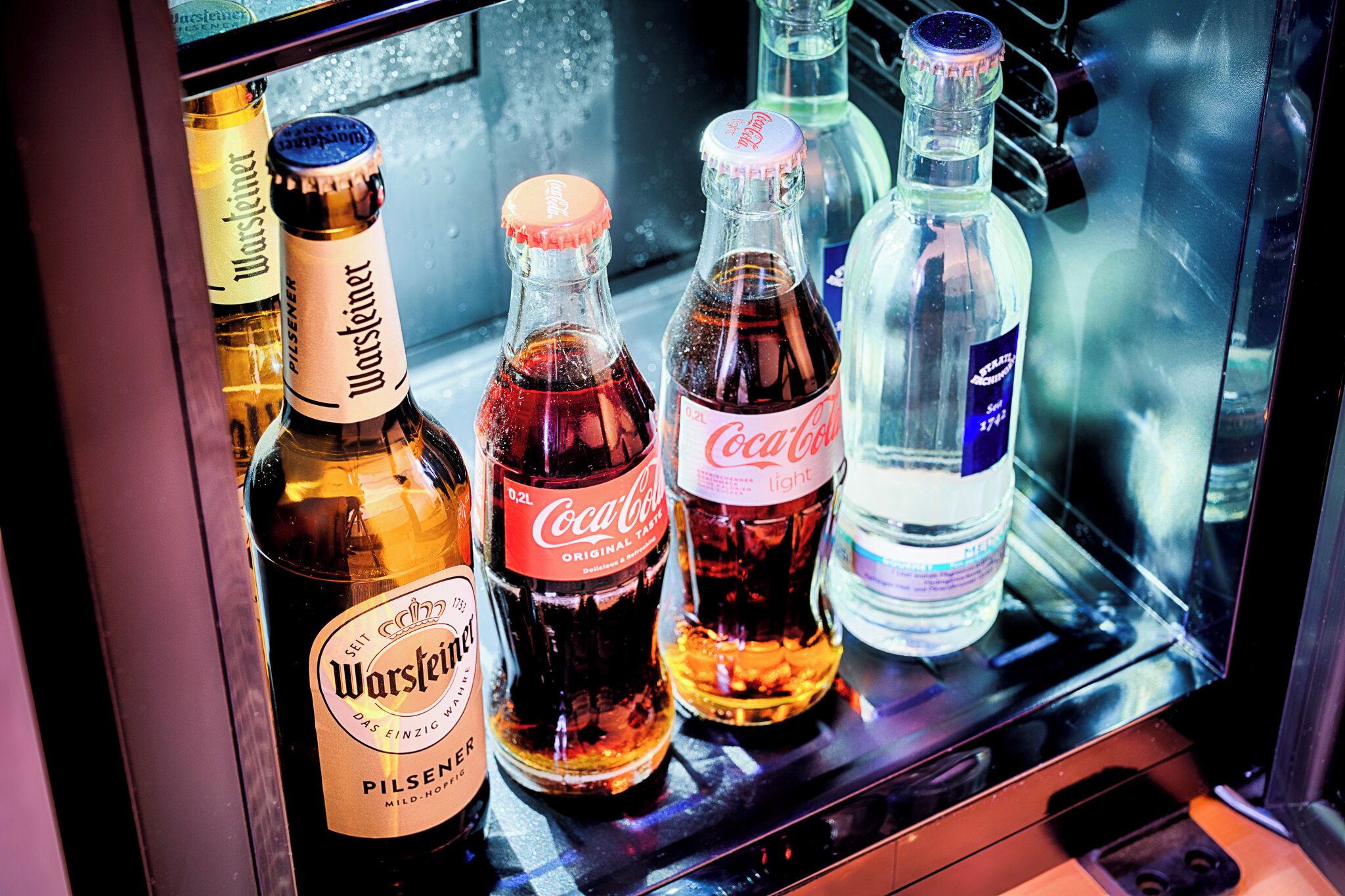 Jääkaappi on täynnä erilaisia juomia, kuten Warsteiner-olutta, Coca-Colaa ja muita virvoitusjuomia.