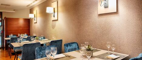 Comedor con mesas dispuestas para cuatro, sillas tapizadas en azul y lámparas de pared.