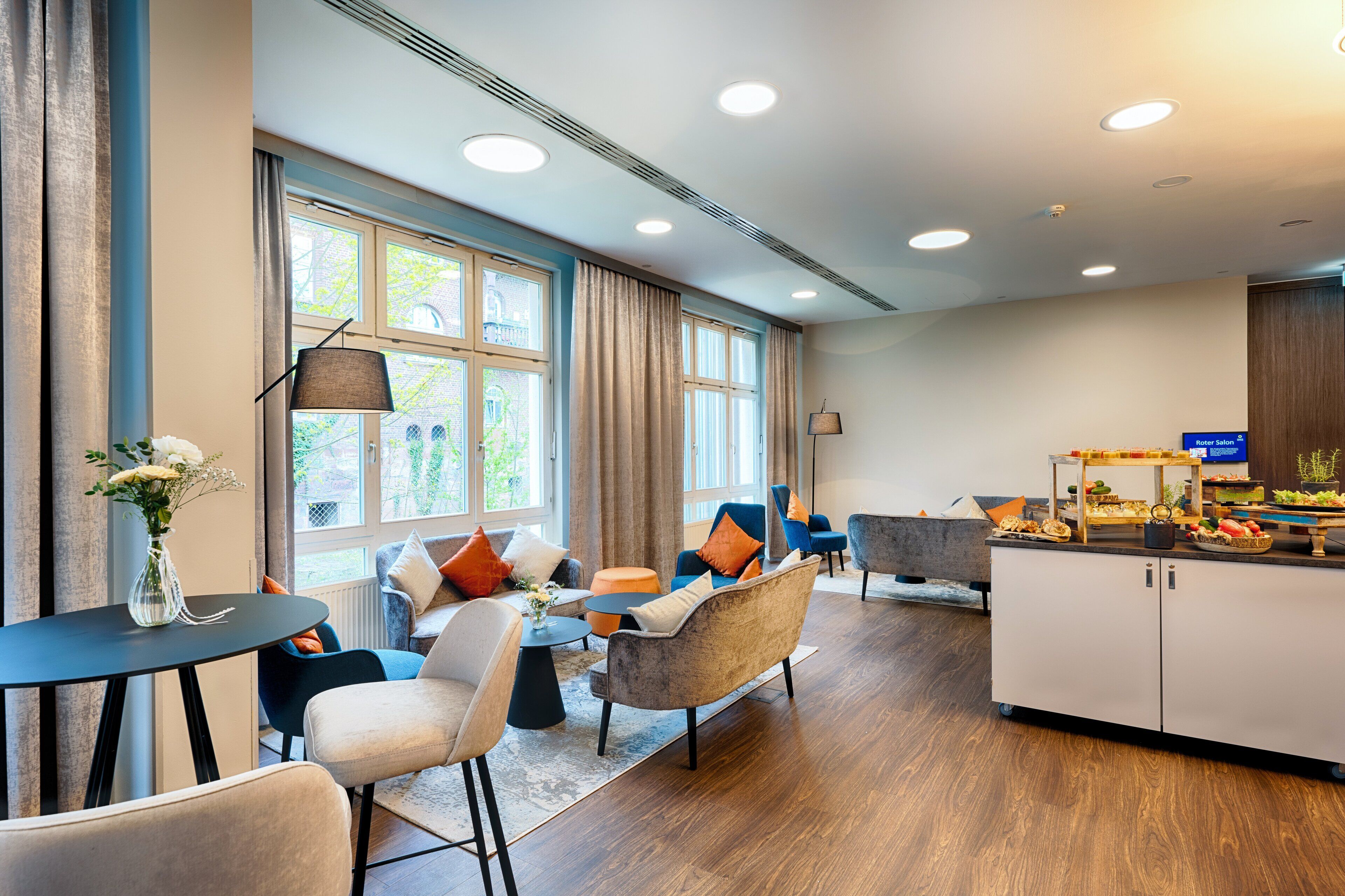 A modern hotel lobby with seating areas, a reception desk, and a buffet.