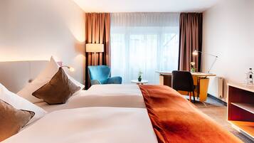 Ein Hotelzimmer mit zwei Betten, einem Schreibtisch, einem Stuhl, einer Lampe und einem kleinen Tisch mit einer Pflanze.