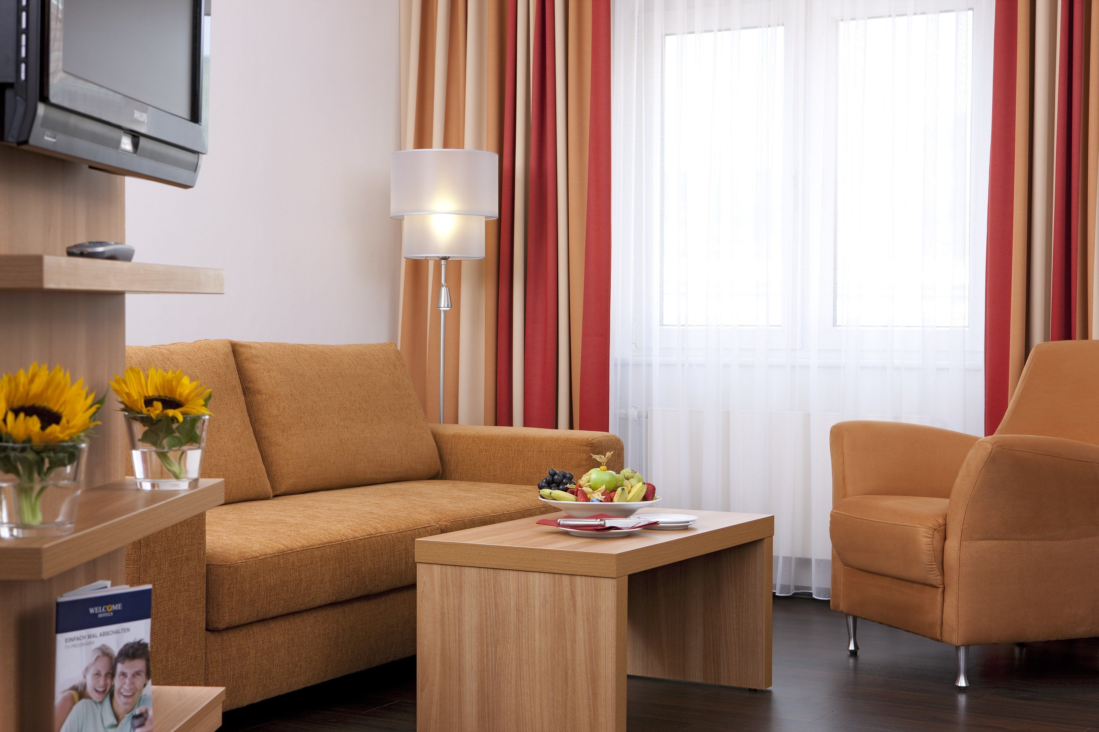 A modern hotel room with a sofa, armchair, and a small table with a fruit bowl.