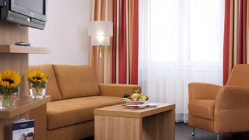 A modern hotel room with a sofa, armchair, and a small table with a fruit bowl.