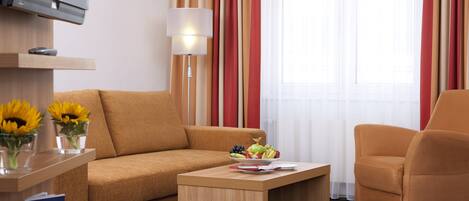 A modern hotel room with a sofa, armchair, and a small table with a fruit bowl.
