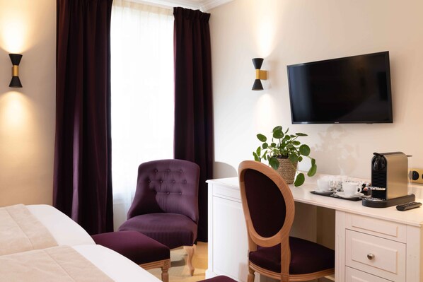 Quarto de hotel com uma cama, uma mesa de trabalho com cafeteira, televisão e uma cadeira.