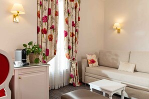 A living room with a sofa, a coffee table, a cabinet, and two wall-mounted lamps. - Hotel Queen Mary Paris (Paris)