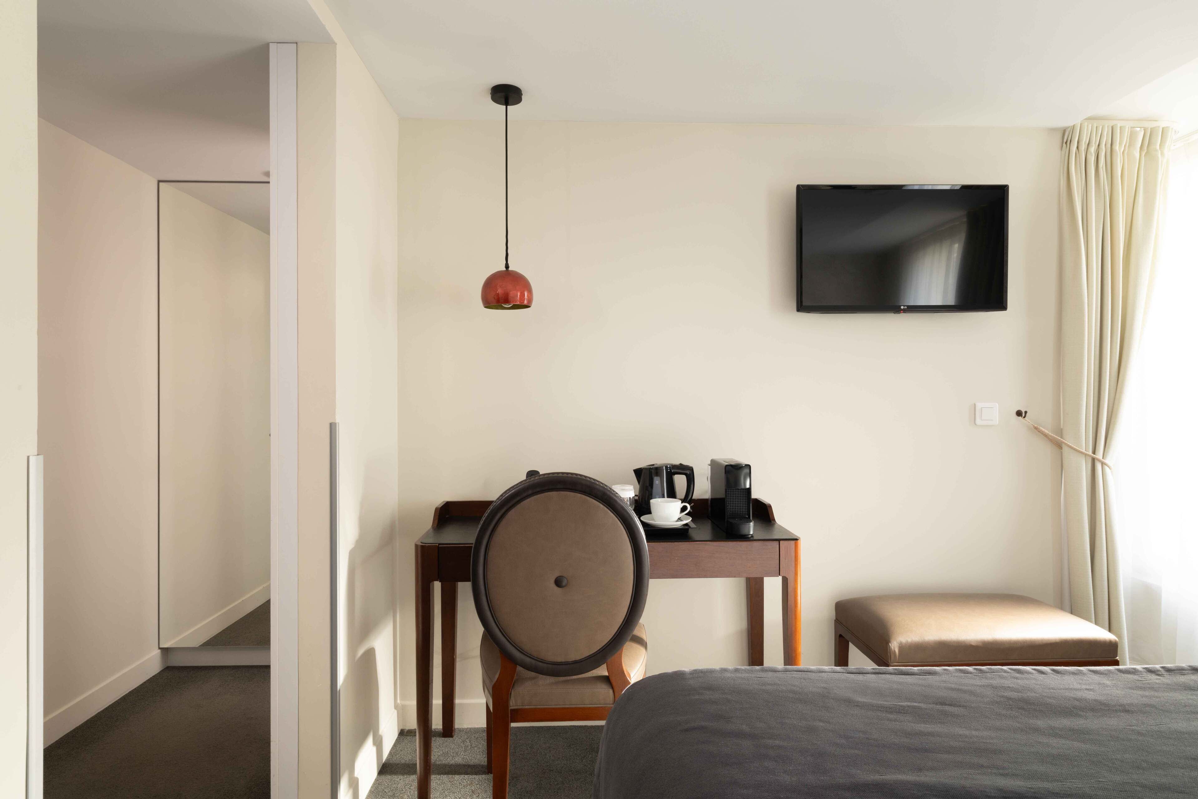 Una habitación de hotel con cama, escritorio, silla, televisor y una mesita con cafetera y taza.