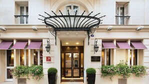 A hotel entrance with a black wrought iron canopy, a sign reading "Queen Mary," and potted plants with pink flowers. - Hotel Queen Mary Paris (Paris)
