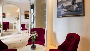 A hotel lobby with red upholstered chairs, a round white table with a vase of flowers, and a framed black and white photograph on the wall. - Hotel Queen Mary Paris (Paris)