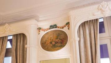 Una habitación con un techo decorativo, un cuadro floral y una puerta con un ventanal circular.