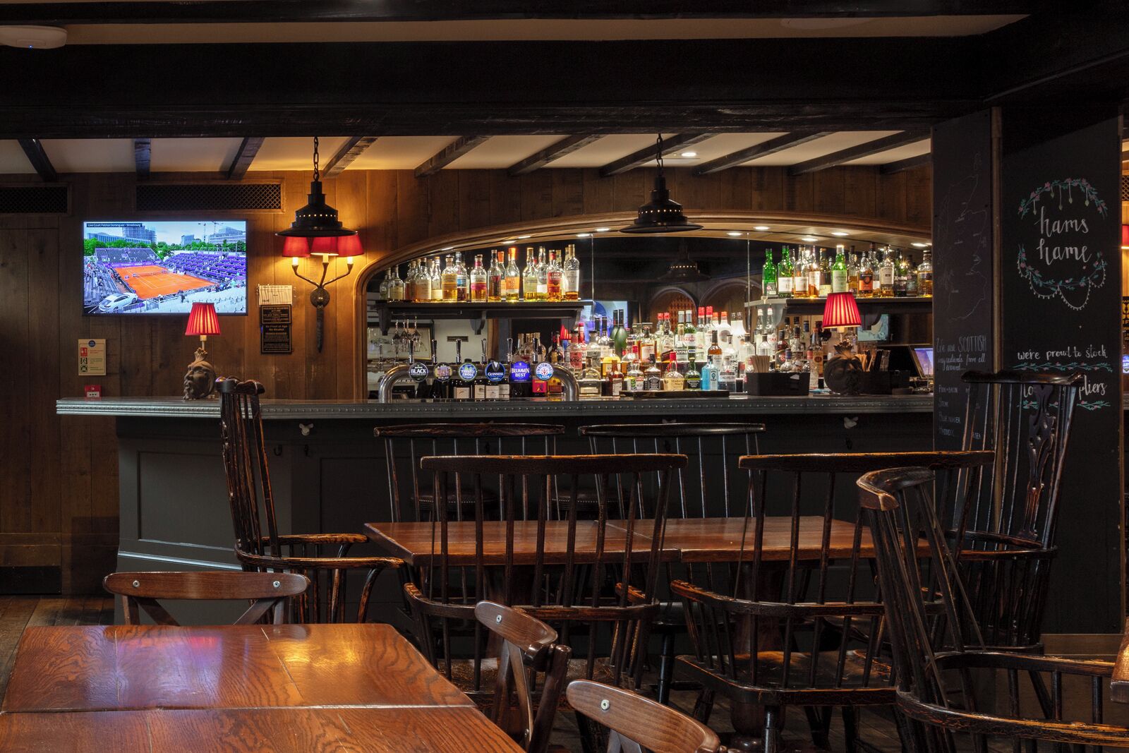 A bar area with wooden furniture, a television screen, and a variety of bottles.