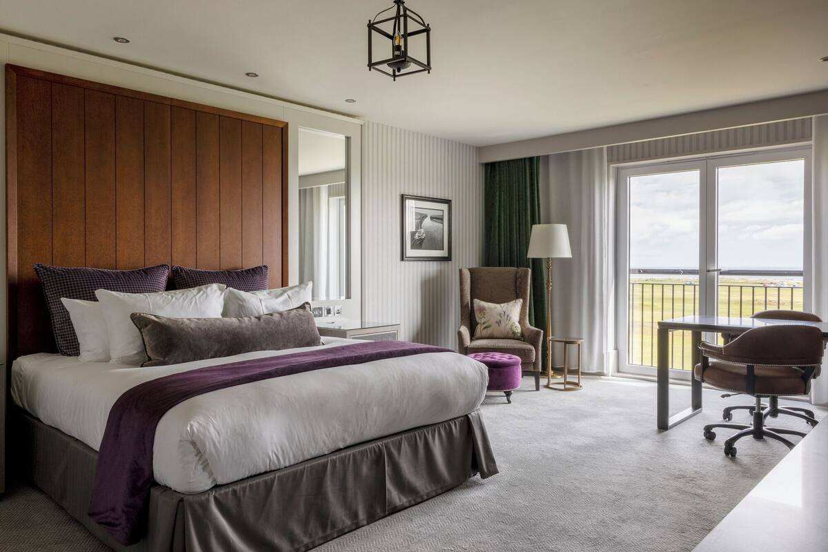 A hotel room with a large bed, a chair, a desk, and a view of the outdoors.