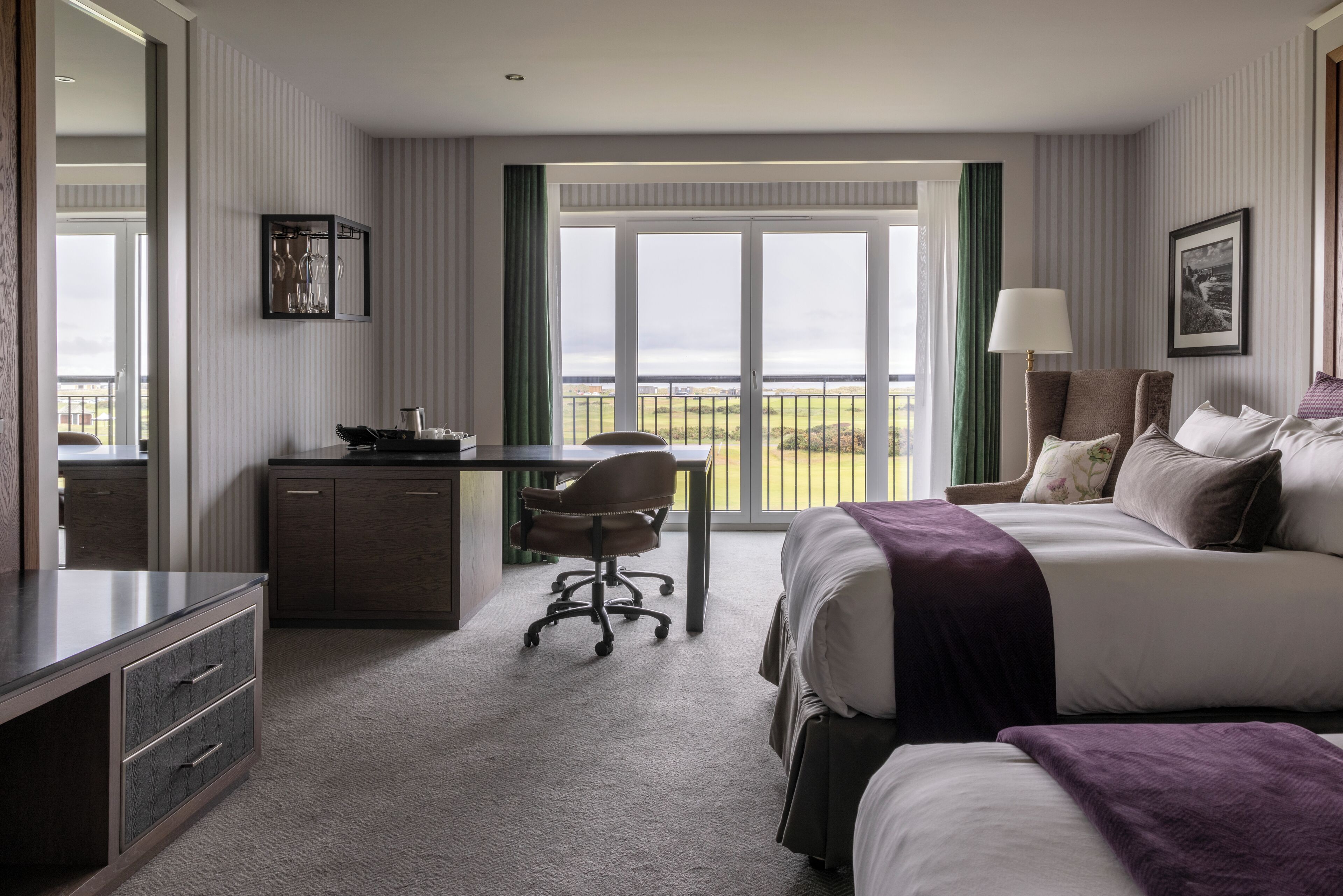 A hotel room with a bed, desk, chair, and a view of the outdoors.