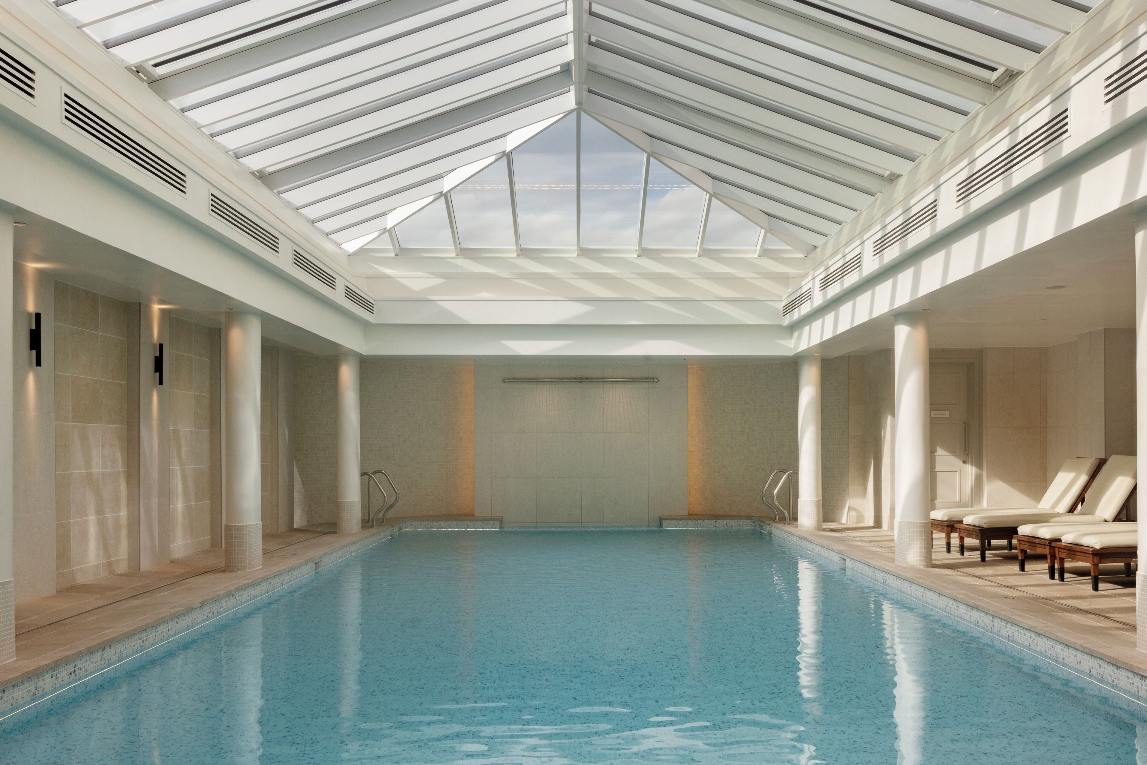 A large indoor swimming pool with a skylight ceiling, surrounded by columns and lounge chairs.