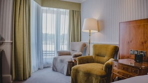 A hotel room with a large window, a lamp, a wooden wardrobe, and a desk with a computer.