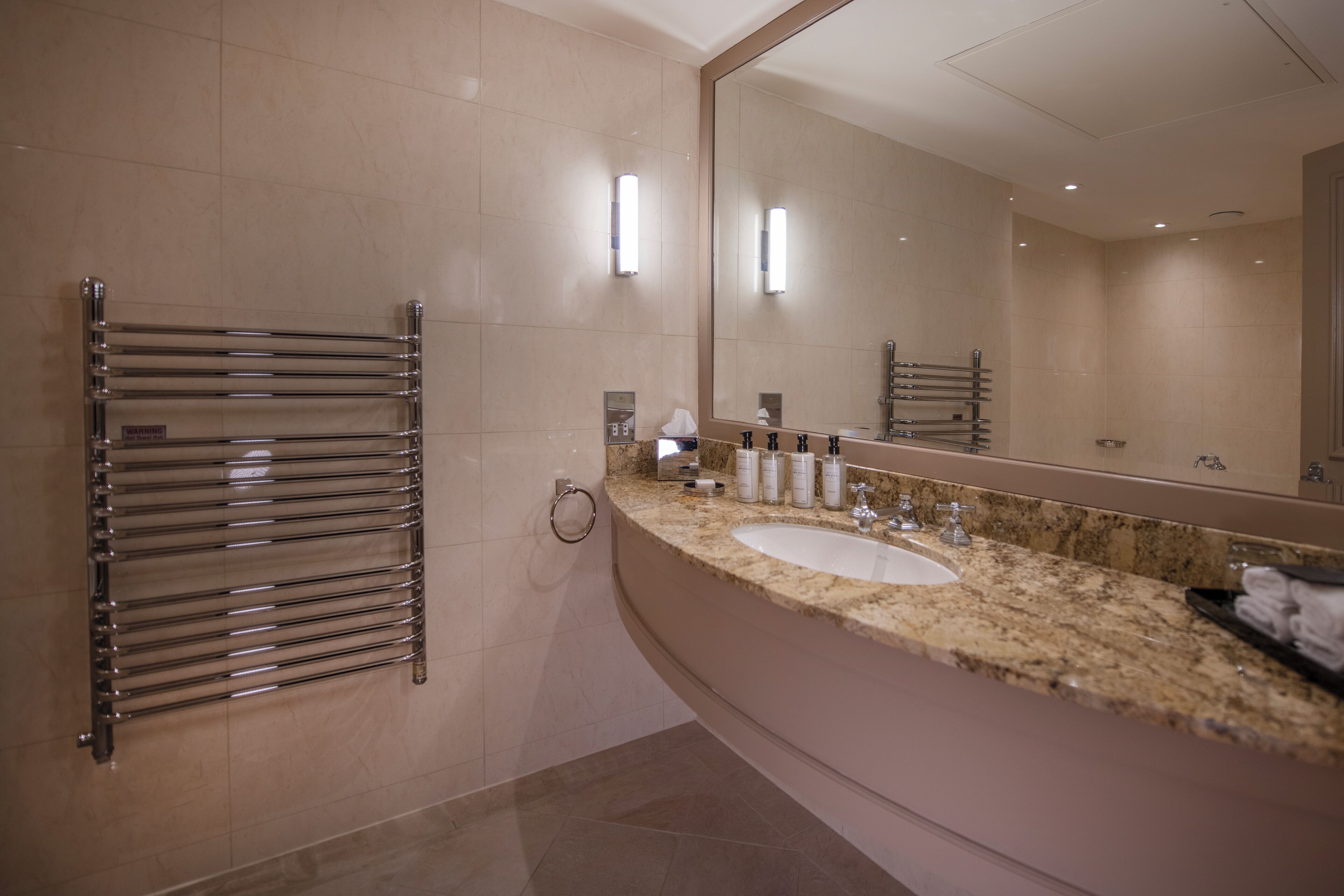 Un baño moderno con un espejo grande, un toallero cromado, una encimera de granito y un lavamanos.