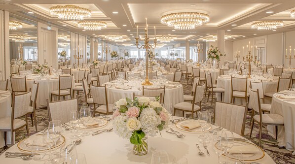 Un salón de banquetes con mesas redondas, sillas y candelabros.