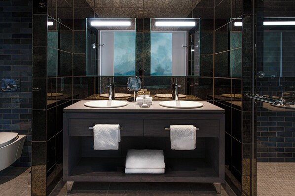 A modern bathroom with two sinks, a glass shower enclosure, and a dark tiled wall.