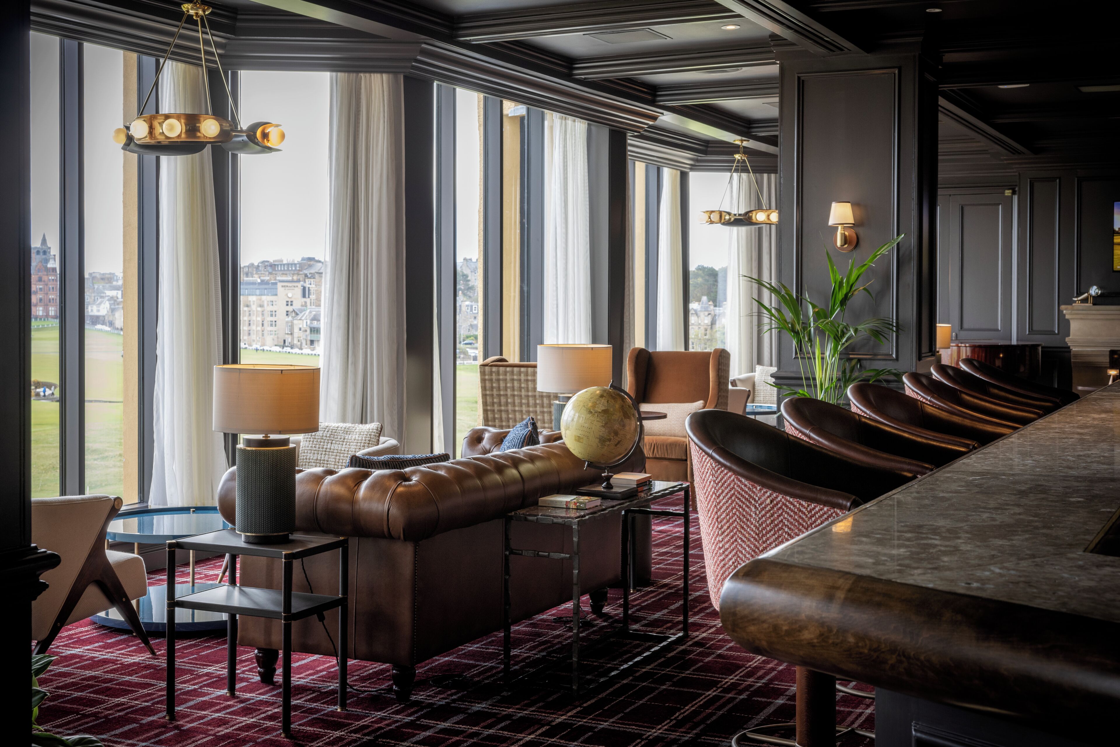 A hotel lobby with a leather sofa, a globe, and a view of the city through large windows.