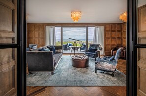 A spacious living room with a large window, a telescope, and a view of the ocean. - Old Course Hotel (St. Andrews)
