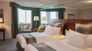 A hotel room with two large beds, a sitting area with a chair, a lamp, and a mirror.