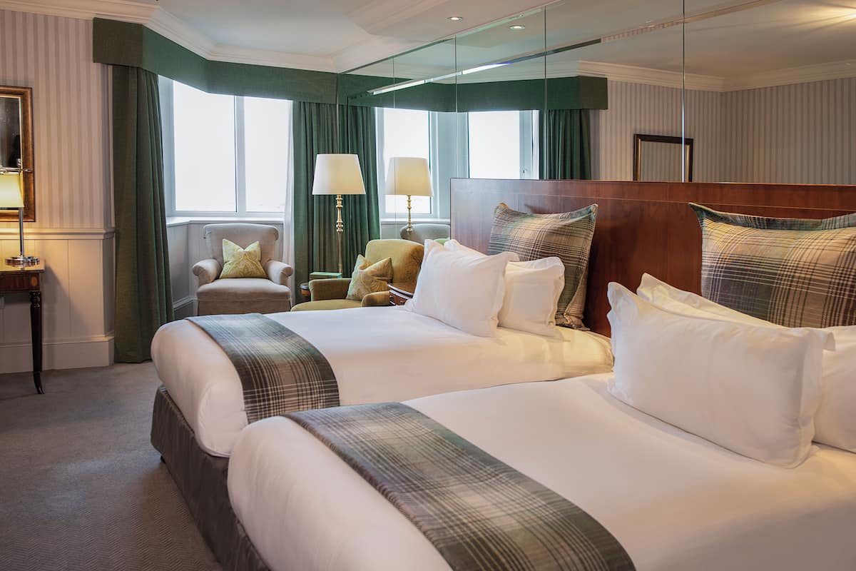 A hotel room with two large beds, a sitting area with a chair, a lamp, and a mirror.