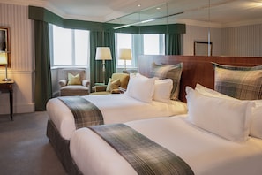 A hotel room with two large beds, a sitting area with a chair, a lamp, and a mirror.