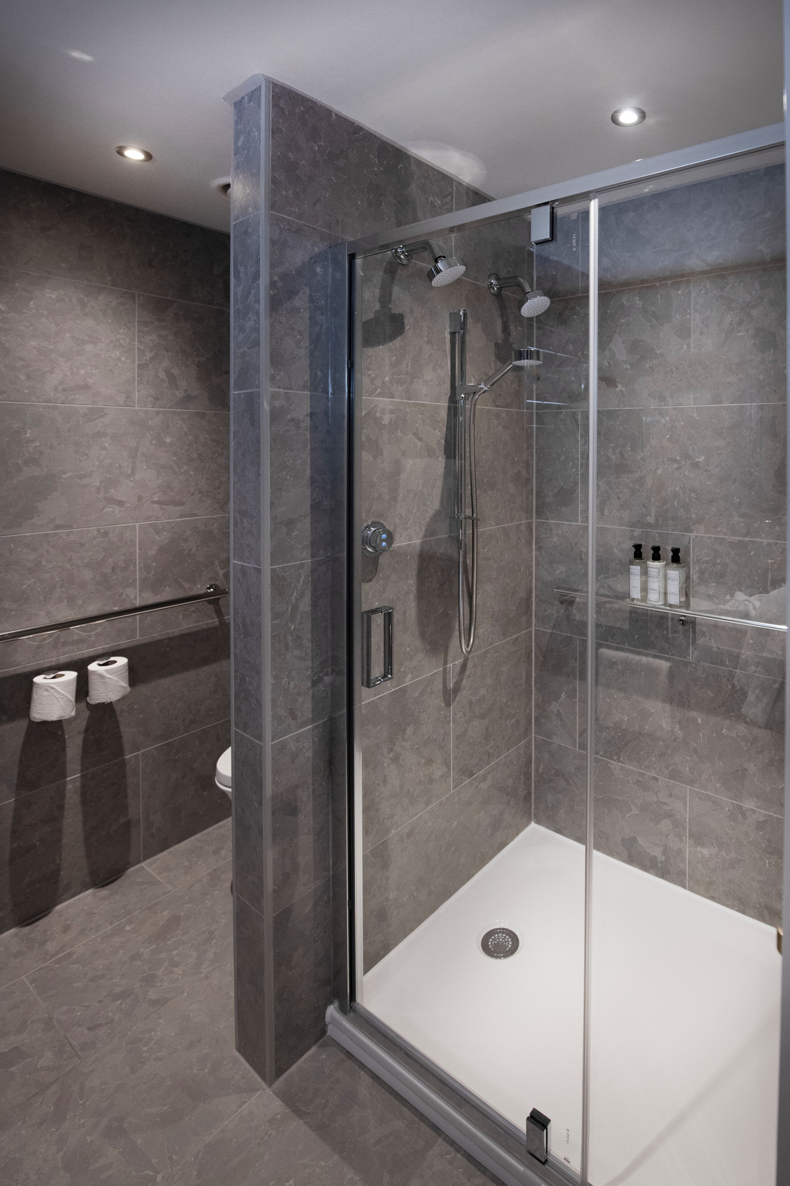 A modern shower area with a glass door, a handheld showerhead, and a wall-mounted faucet.