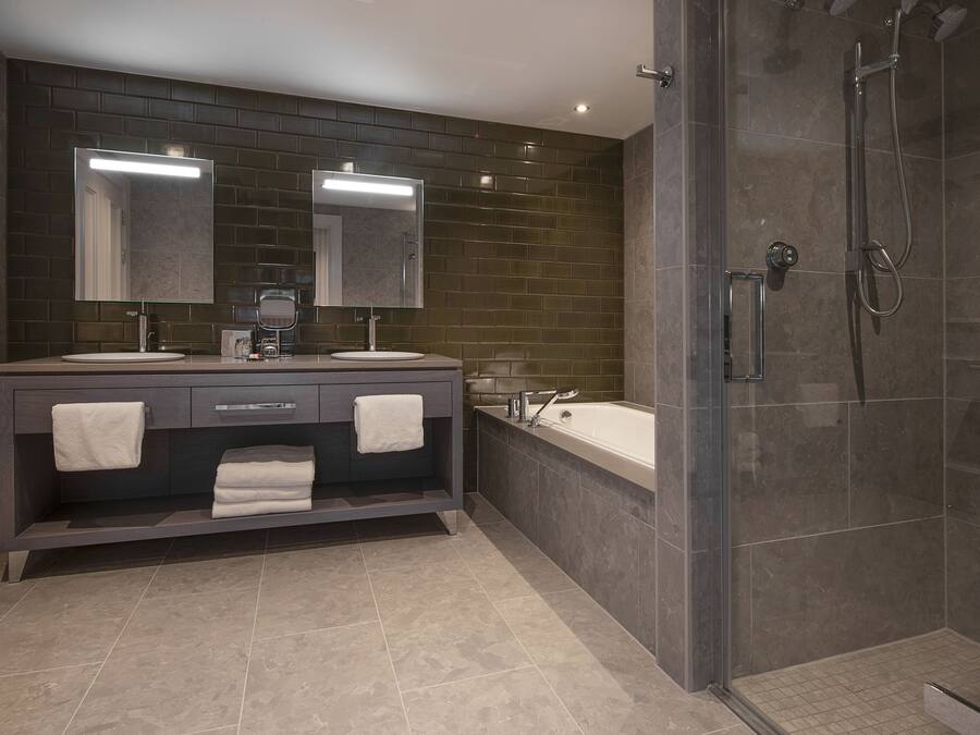 Un baño moderno con dos lavamanos, un espejo grande, una bañera y un área de ducha con mampara de vidrio.