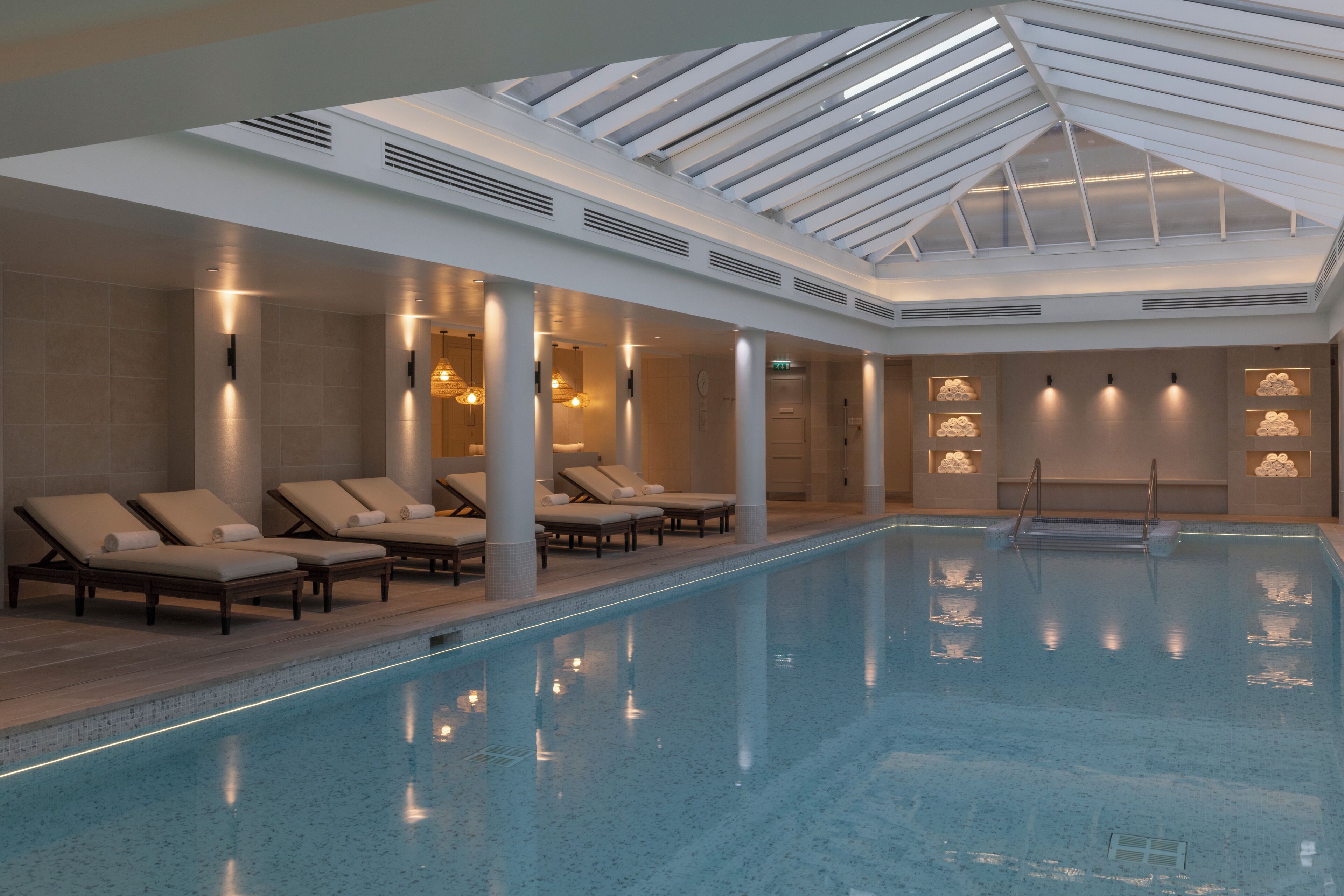A large indoor swimming pool with lounge chairs and a skylight ceiling.