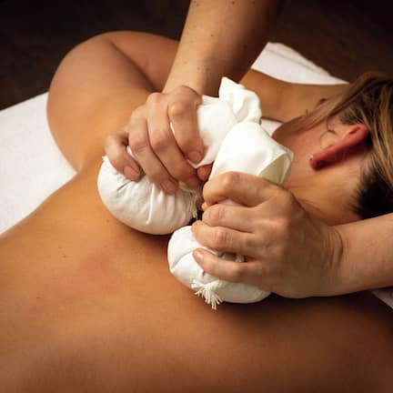 A person receiving a massage with a white towel and a rolled-up towel on their back.