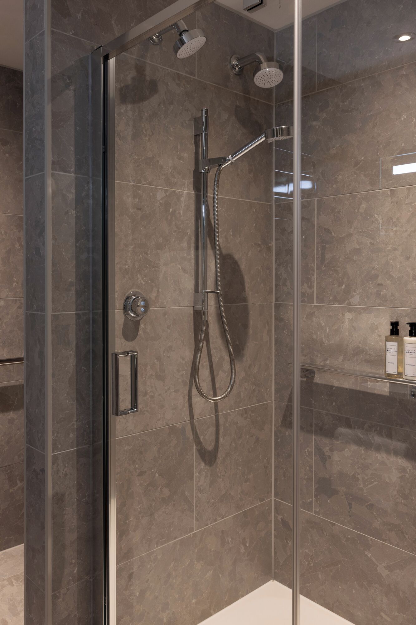 A modern shower enclosure with a glass door, a handheld showerhead, and a wall-mounted showerhead.