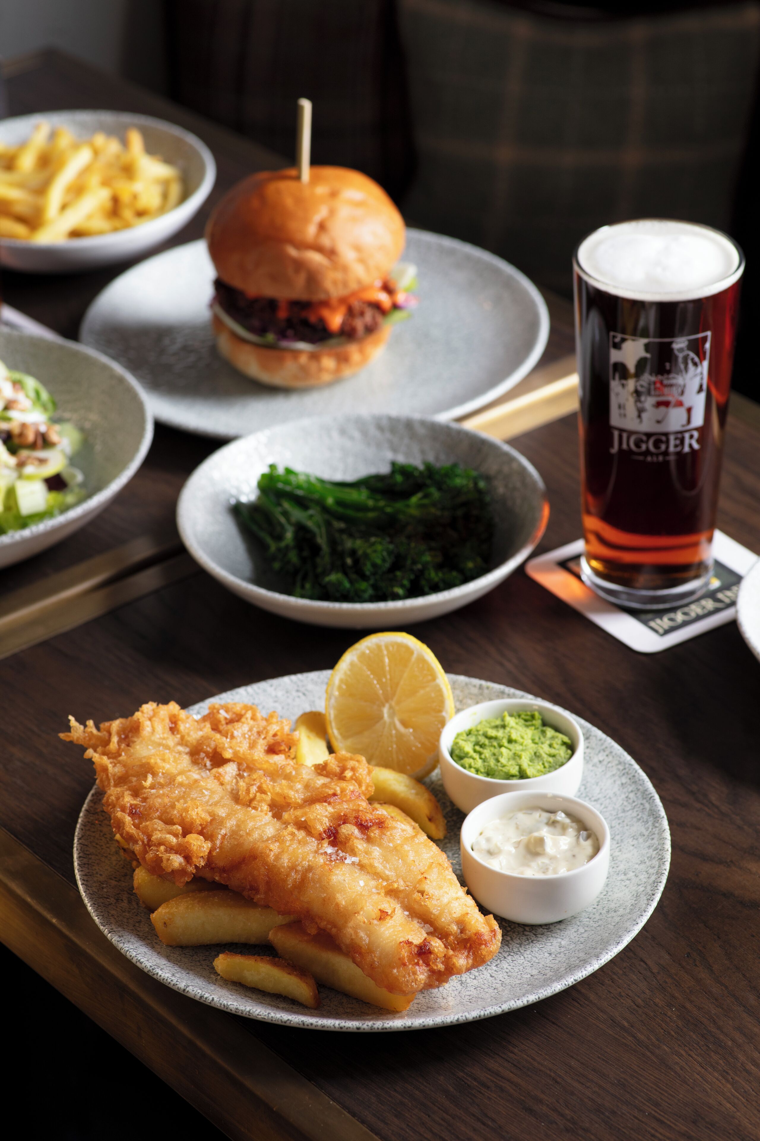 A meal with fish and chips, a burger, and a beer on a table.