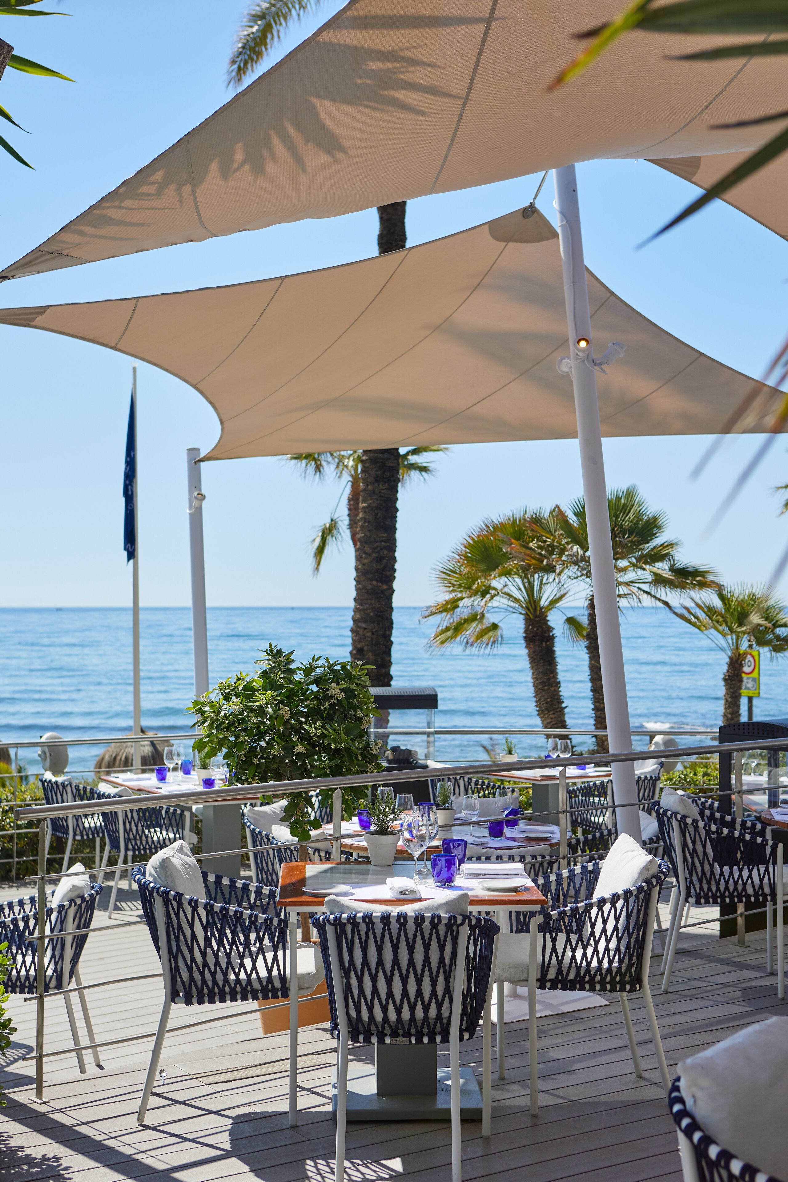 Un espace extérieur aménagé pour les repas, avec des tables et des chaises, offrant une vue sur la mer.
