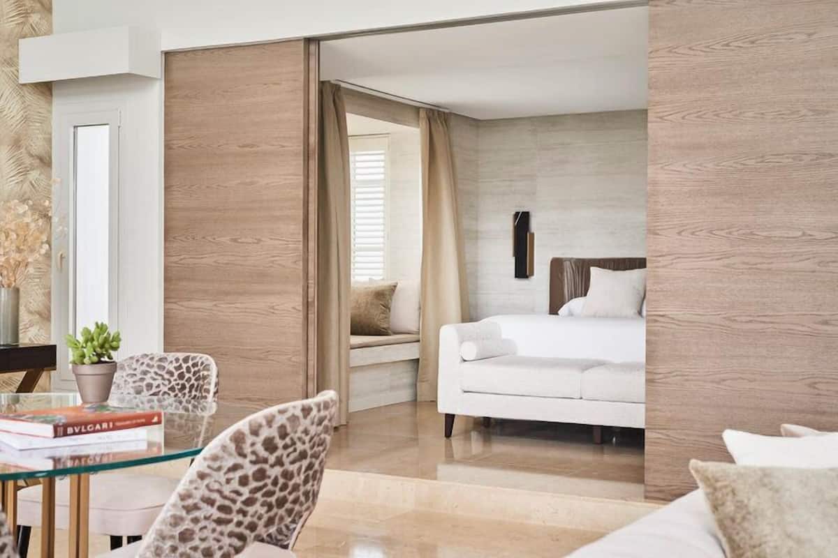 A modern bedroom with a white bed, a glass table with books, and a leopard print chair.