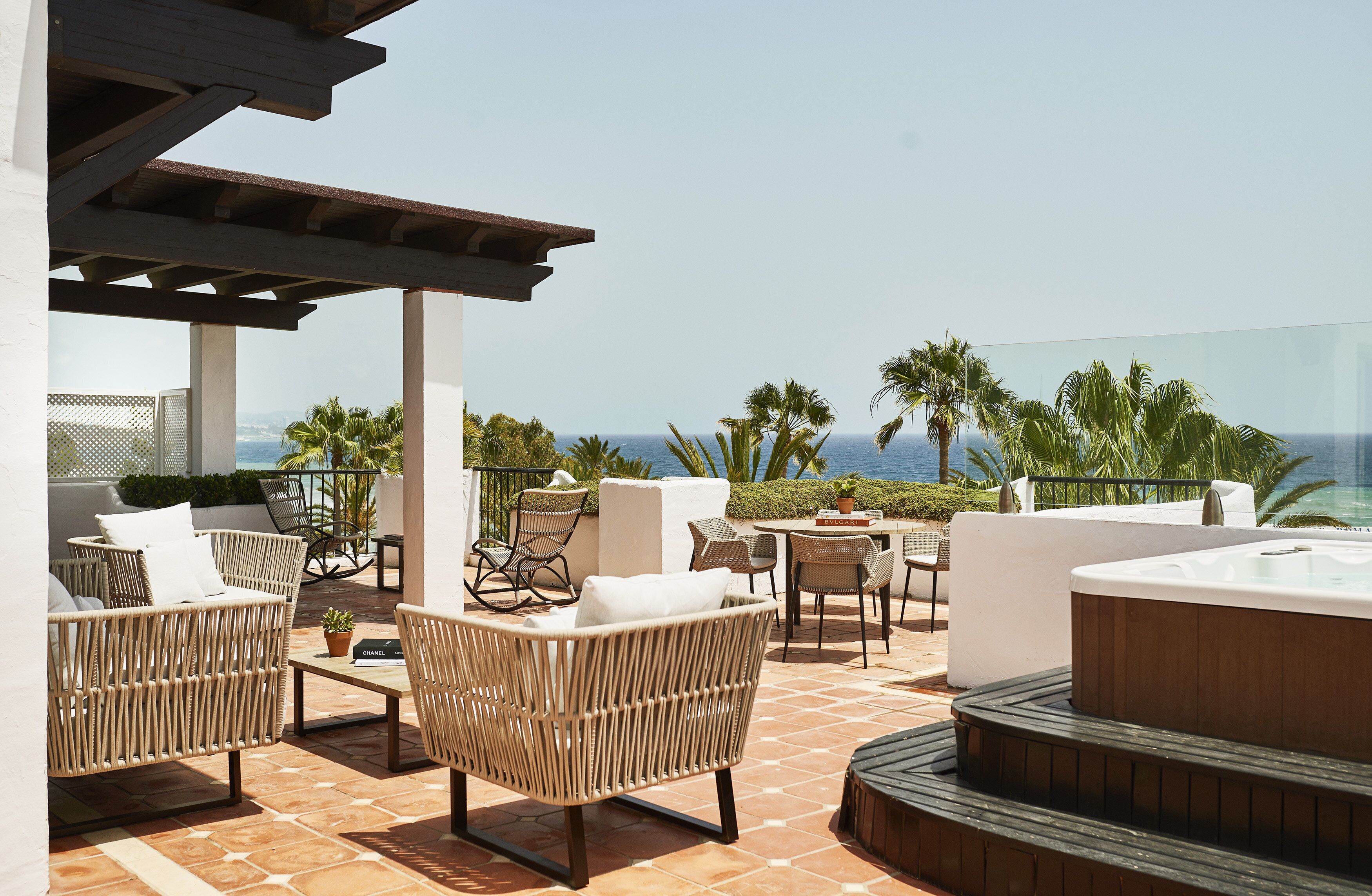 A rooftop terrace with wicker furniture, a hot tub, and a view of the ocean.