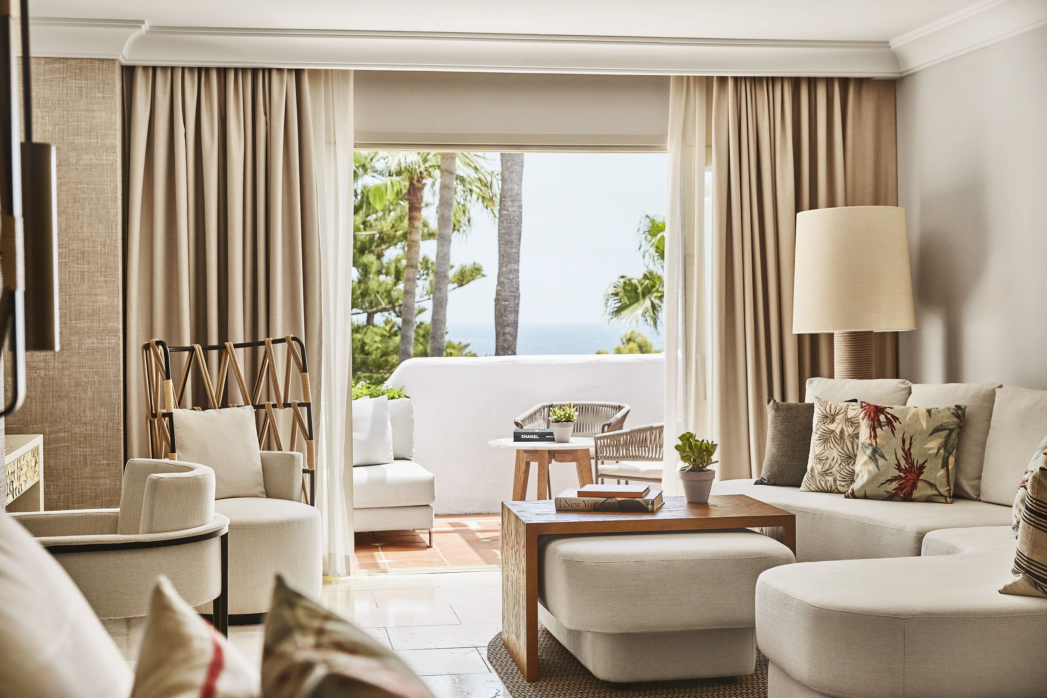 A modern hotel room with a sofa, armchairs, a coffee table, and a view of the ocean.