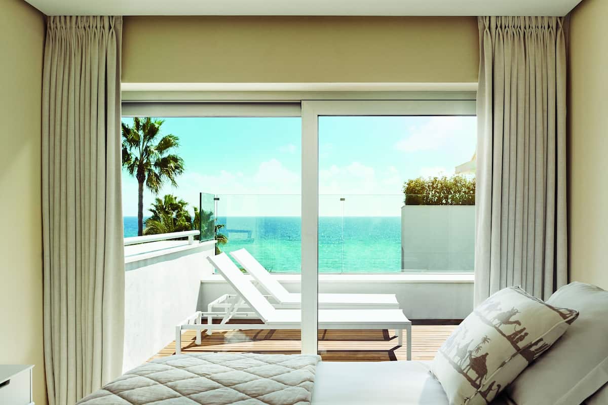 A hotel room with a bed, a TV, and a balcony with a view of the ocean.